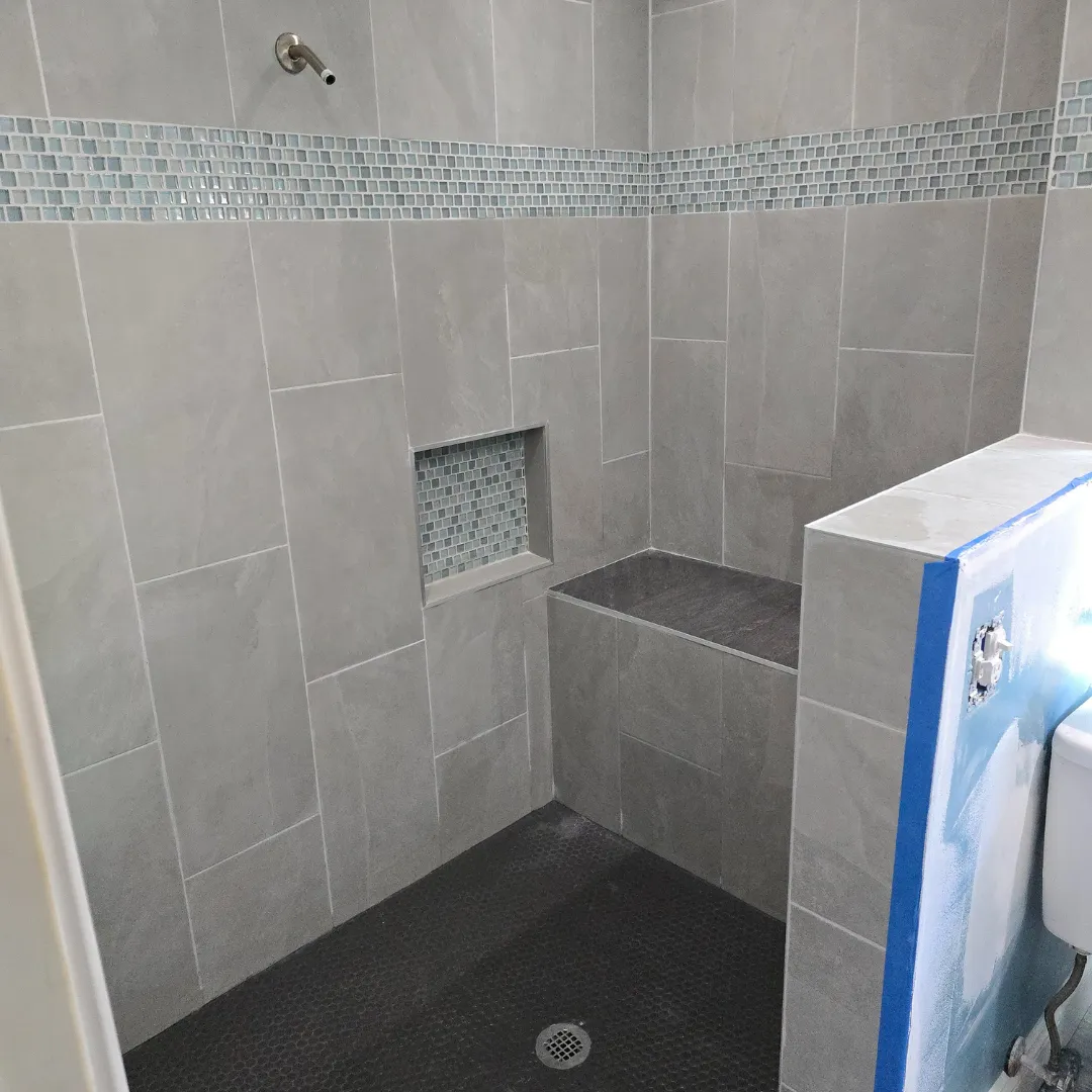 Light gray porcelain shower with glass mosaic band and built-in bench by Link Services Pro in Shrewsbury, MA