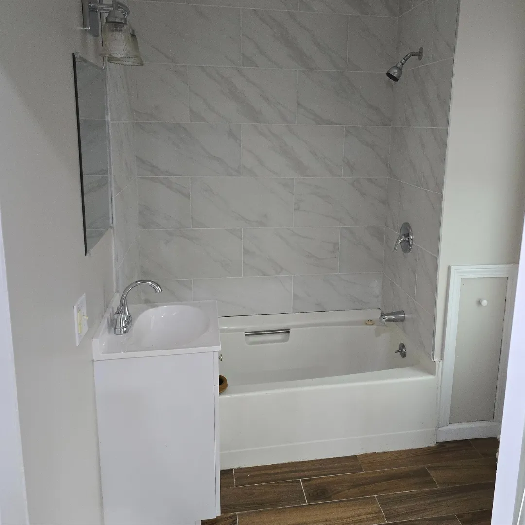 Tub-shower combo with white marble-look subway tile and floating vanity by Link Services Pro in Holden, MA