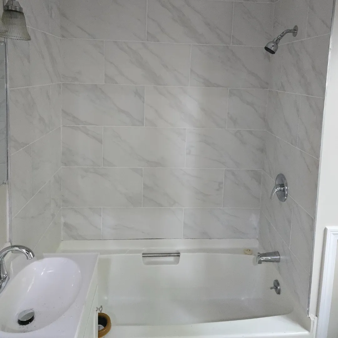 Bright bathroom with white marble-look tile shower surround and wood-look porcelain by Link Services Pro in Worcester, MA