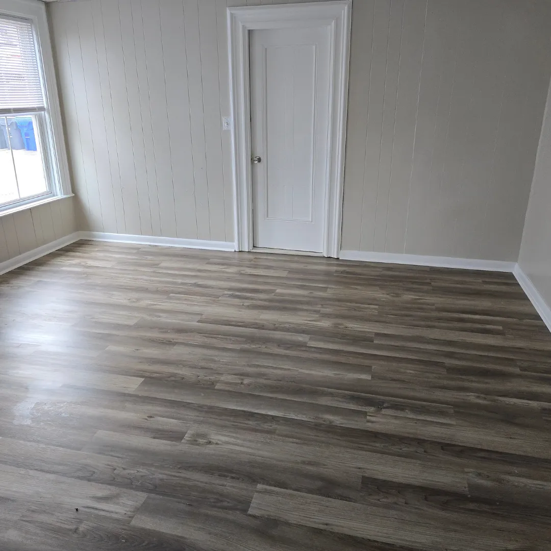 Gray vinyl plank flooring in empty room with white painted trim by Link Services Pro in Auburn, MA