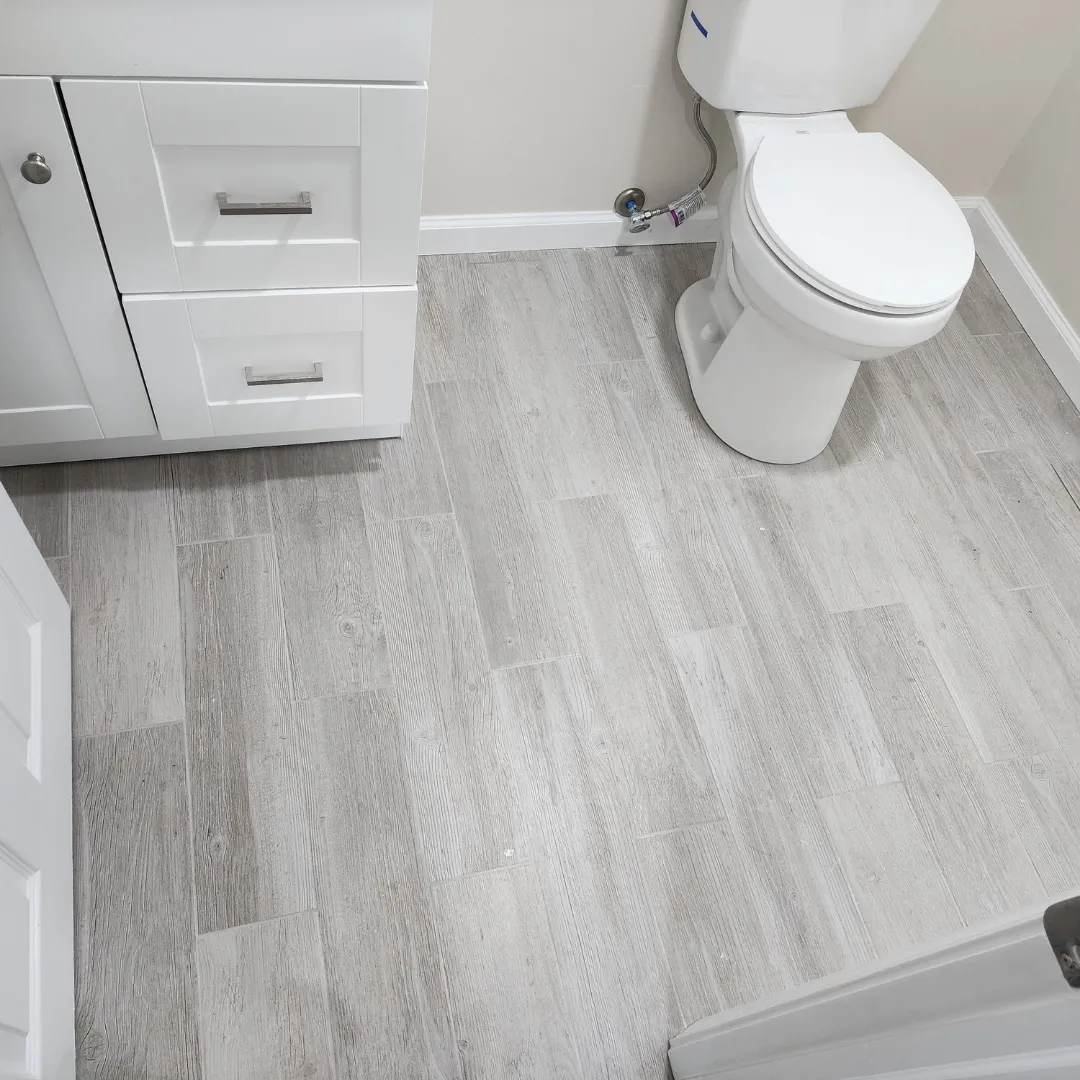 Wood-look porcelain tile flooring in compact bathroom with white vanity by Link Services Pro in Shrewsbury, MA