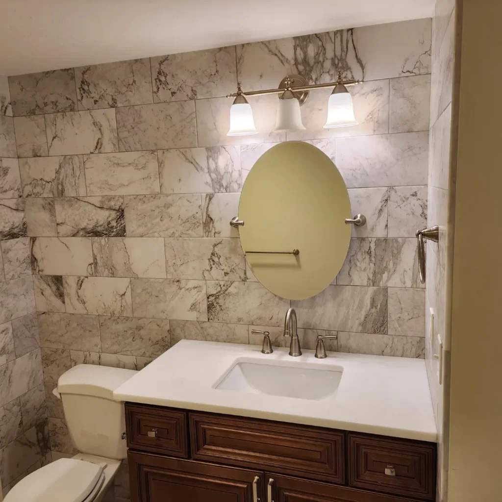 Bathroom remodel with veined marble-look porcelain wall tile and oval mirror by Link Services Pro in Millbury, MA