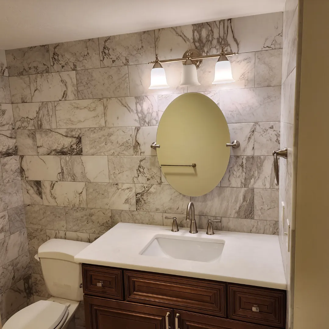 Bathroom remodel with veined marble-look porcelain wall tile and oval mirror by Link Services Pro in Millbury, MA