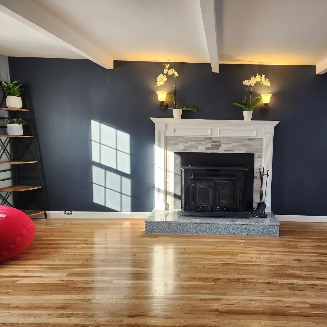 Living room with navy walls, white fireplace mantle and refinished hardwood floor by Link Services Pro in Millbury, MA
