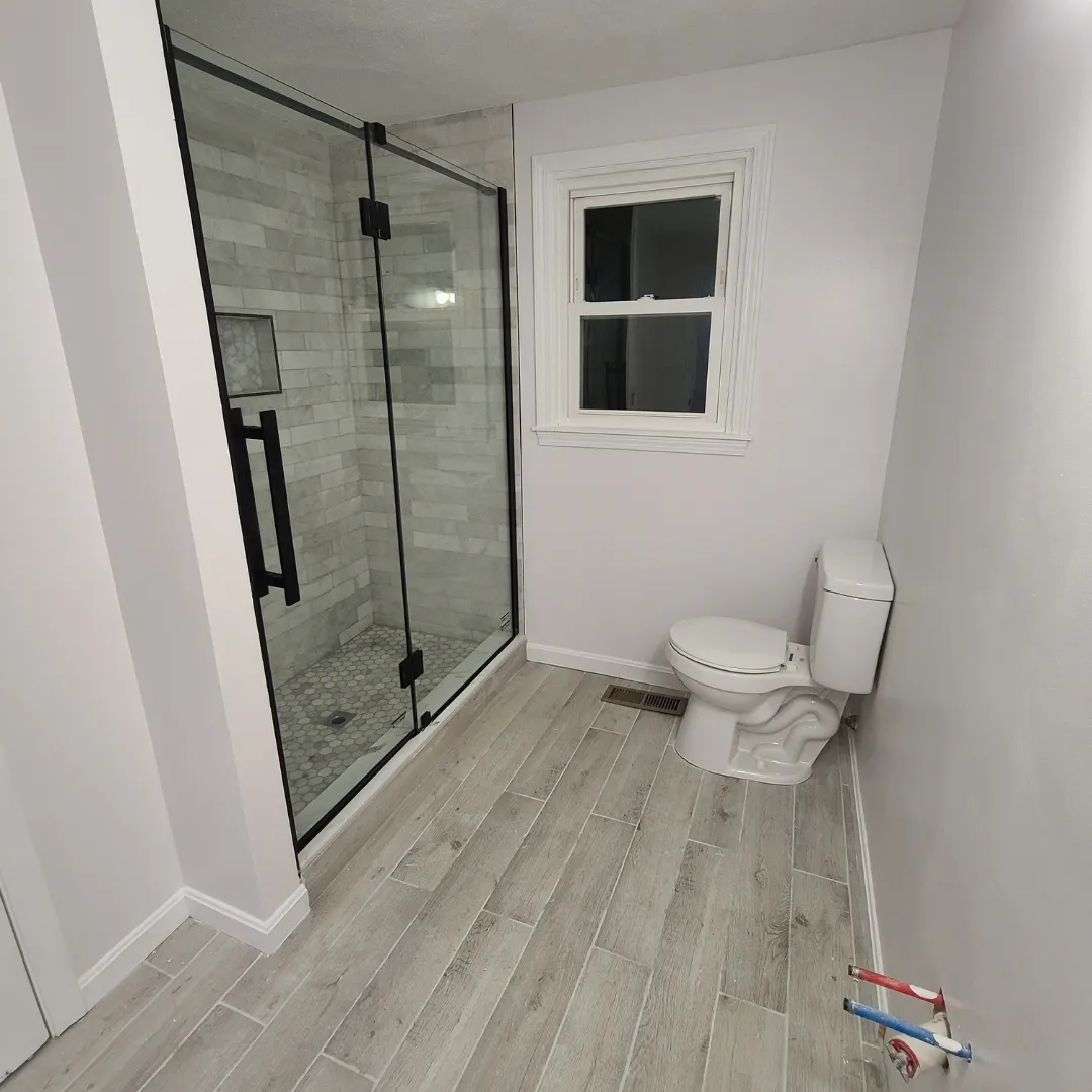 Bathroom with frameless glass shower enclosure and wood-look porcelain floor by Link Services Pro in Millbury, MA
