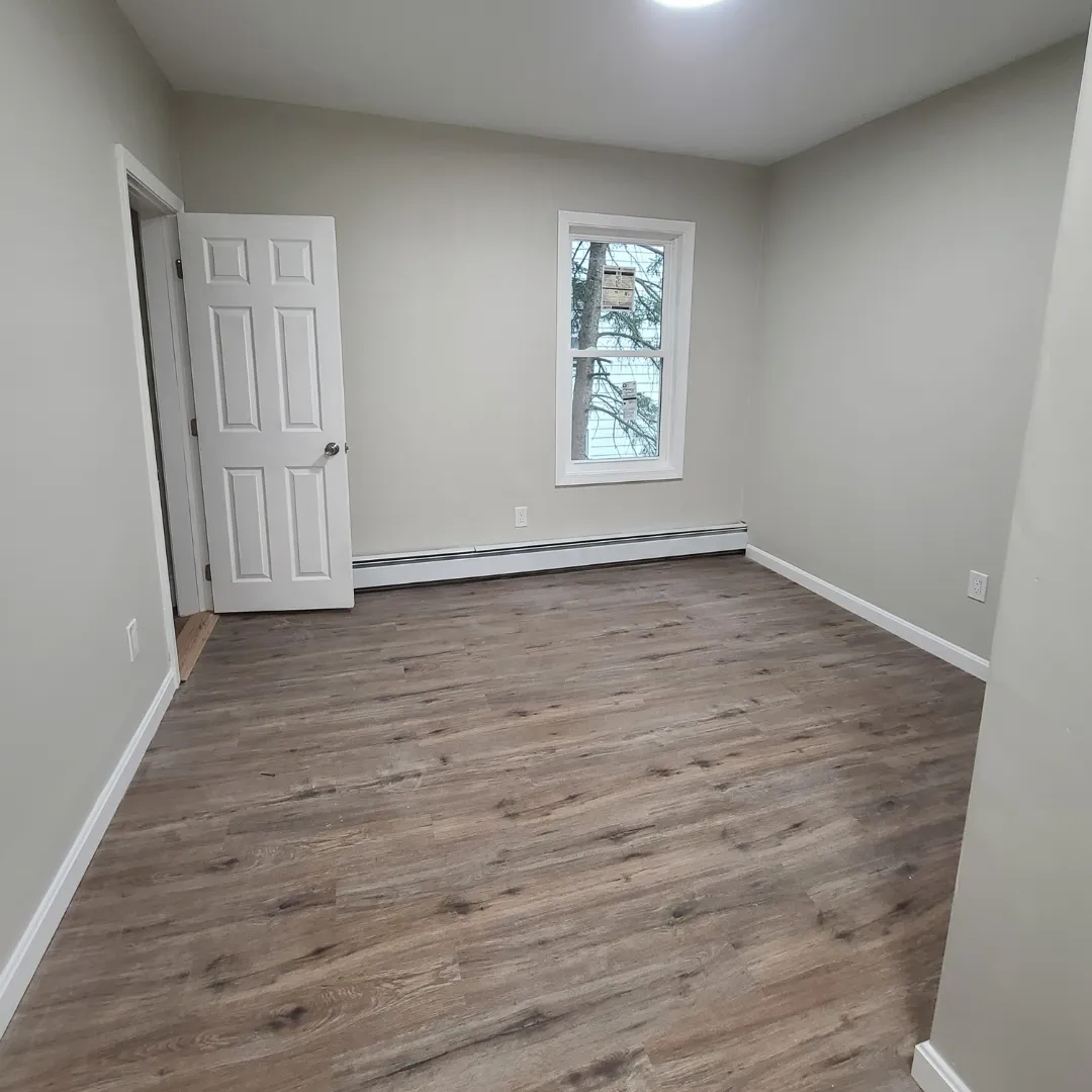 Empty bedroom with rustic gray vinyl plank flooring and fresh white trim by Link Services Pro in Auburn, MA