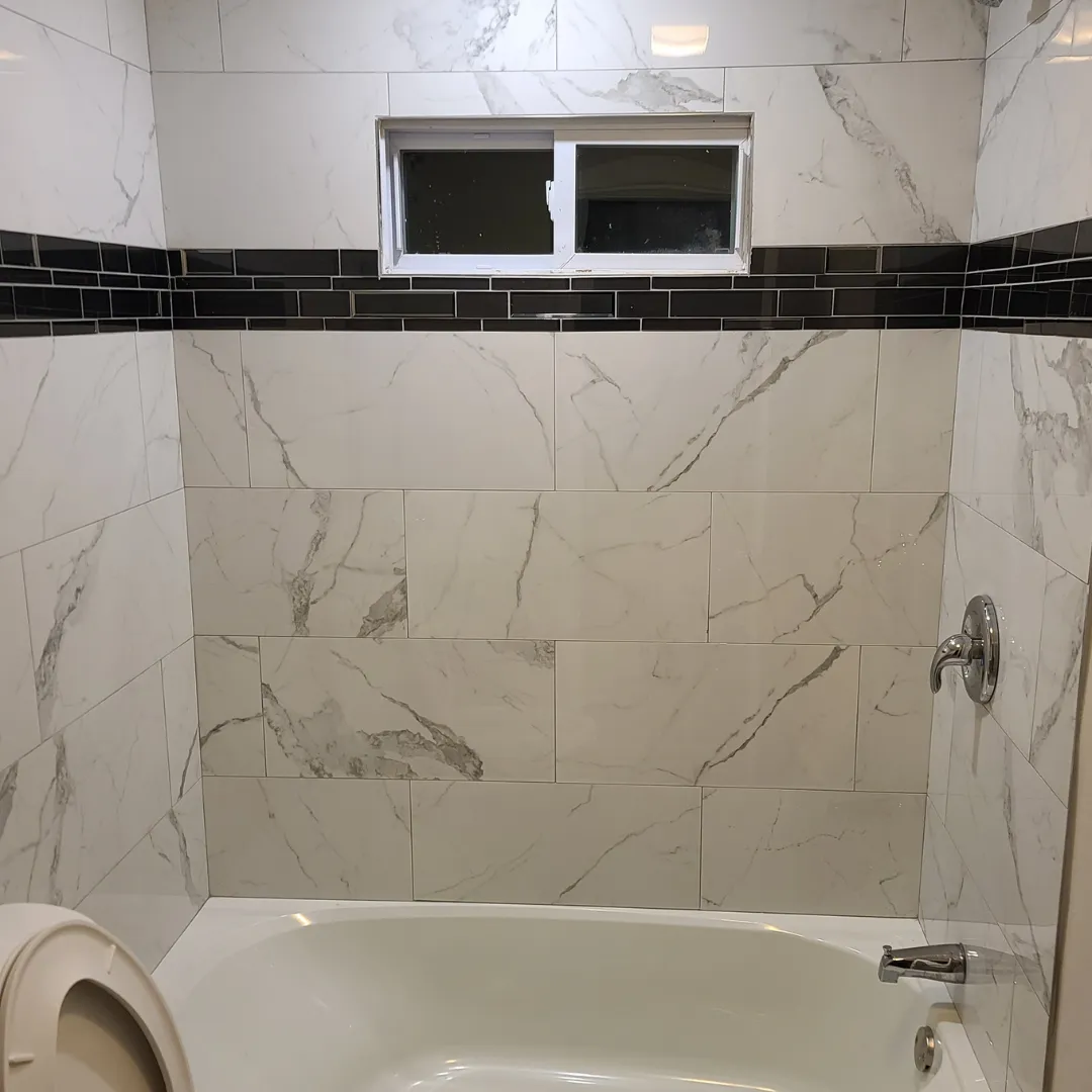 Tub surround in white marble-look porcelain with black glass mosaic stripe by Link Services Pro in Worcester, MA