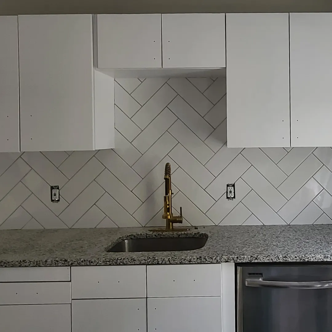White herringbone subway tile backsplash with brass faucet over granite by Link Services Pro in Auburn, MA