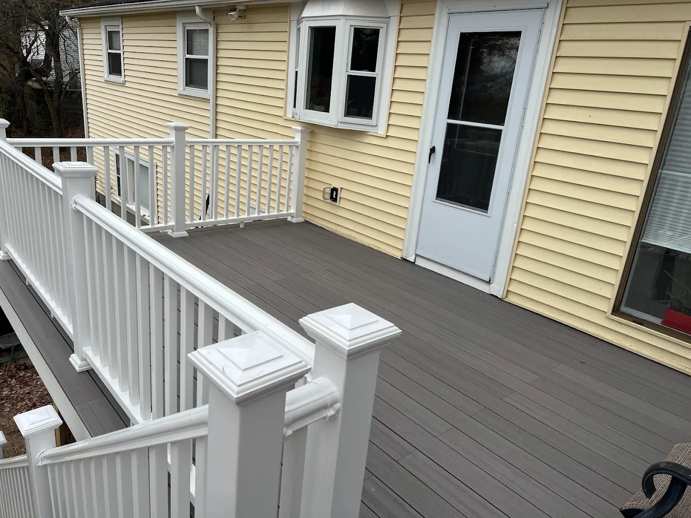 New grey composite deck boards and white vinyl railings installed on a yellow house. by Link Services Pro Inc in Worcester, M