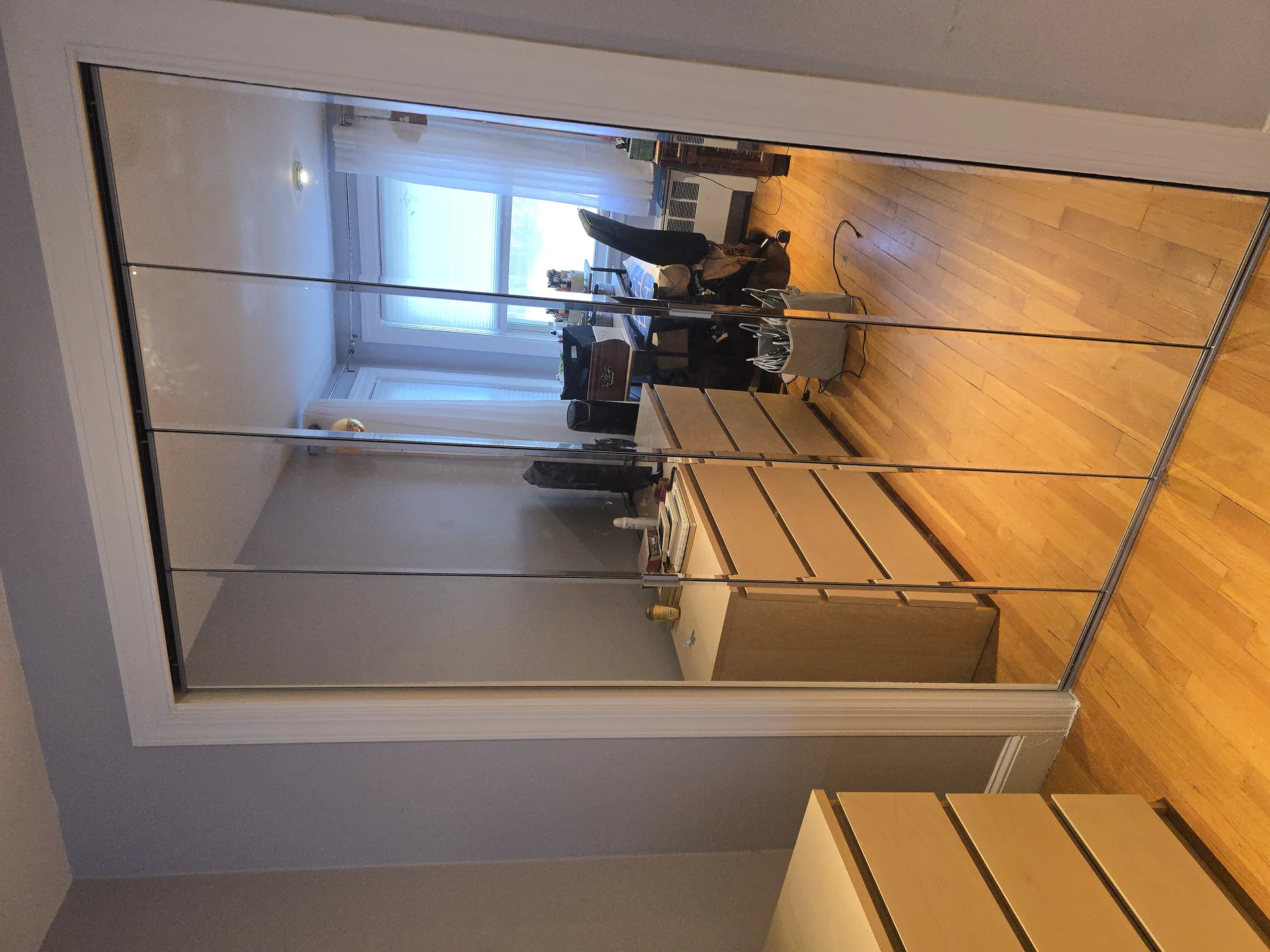 Mirrored closet doors reflecting an office space with hardwood floors and light gray walls. by Link Services Pro Inc in Westb