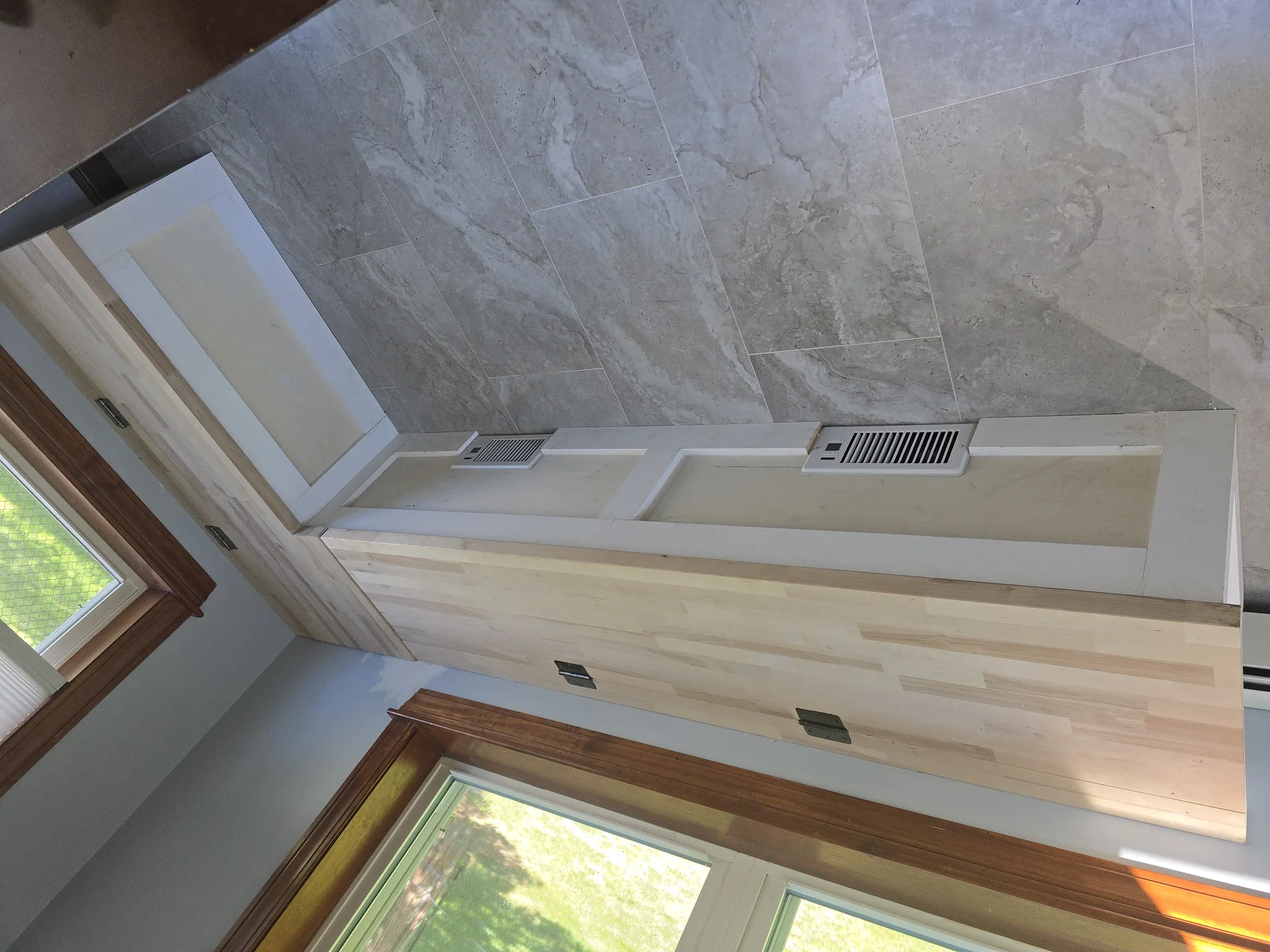 Light gray large format tile flooring next to light wood cabinetry and white trim. by Link Services Pro Inc in Auburn, MA